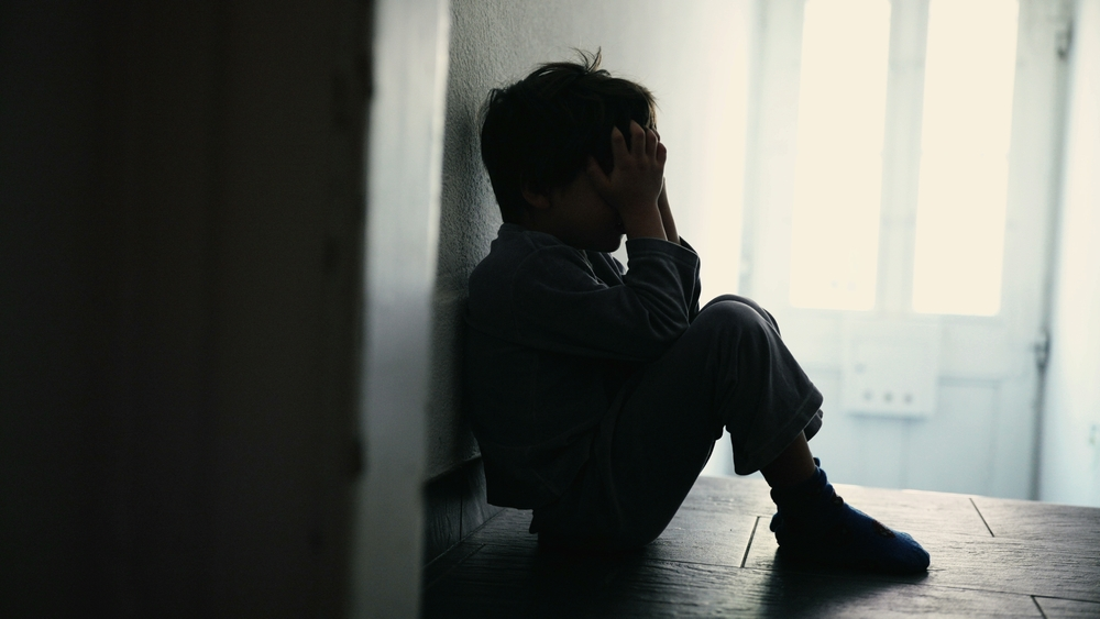 young boy sitting in the dark representing a child sexually abused in the foster care system