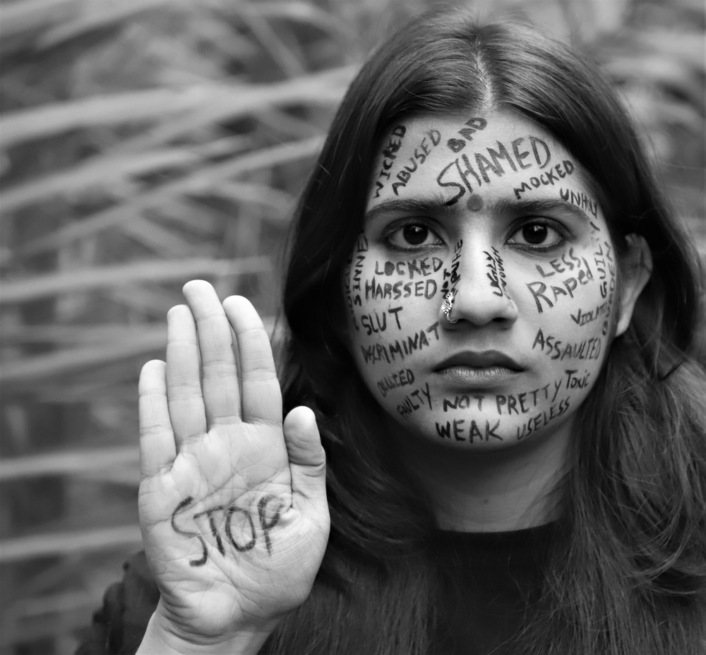 A brown young woman protesting against violence against women and girls by writing messages on her face ,asking to stop violence
