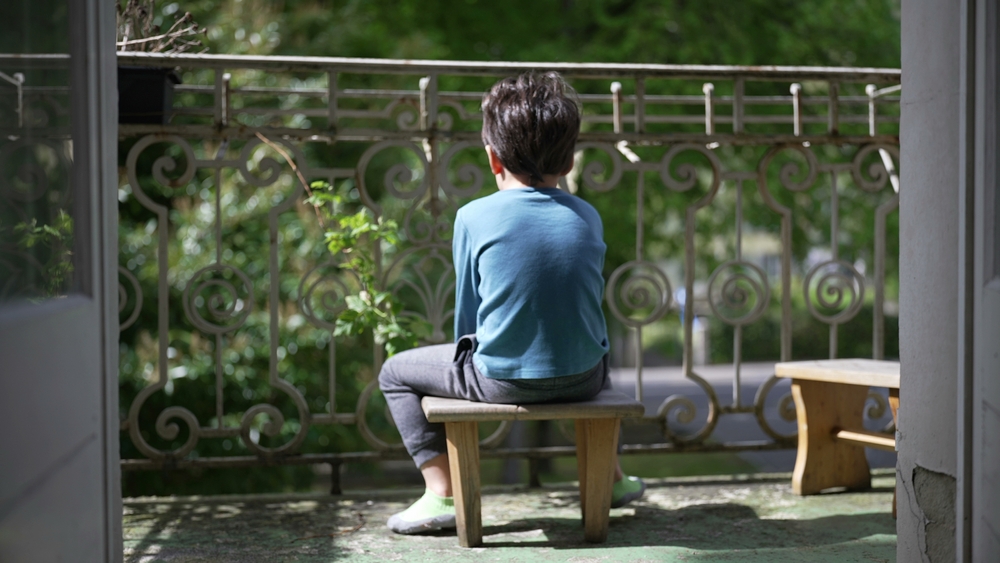 Young boy sitting quietly on a balcony stool, facing away, enjoying a peaceful moment outdoors. the solitude and calmness of a child reflecting in a serene environment