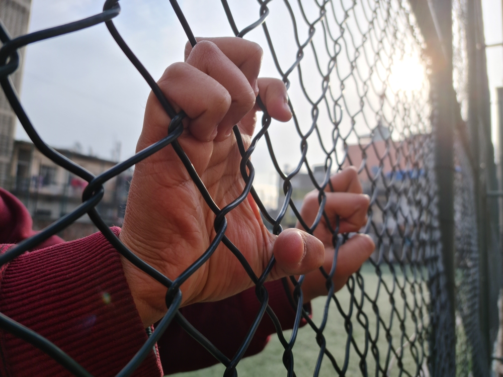Close-up of juvenile detainee’s hands holding a chain-link fence at a youth detention center, symbolizing confinement and institutional abuse claims by File Abuse Lawsuit